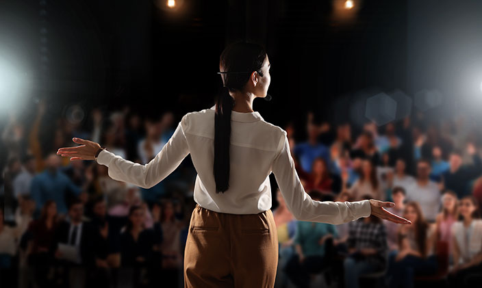 The back of a business woman speaking to a large crowd