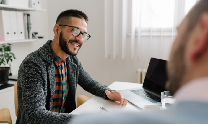 Man at desk speaking with co-worker across from him