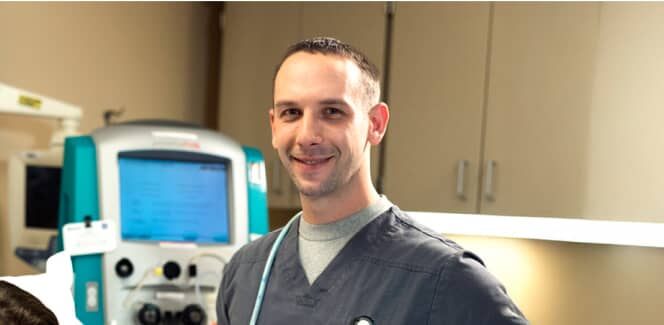 A healthcare worker standing and smiling in grey scrubs