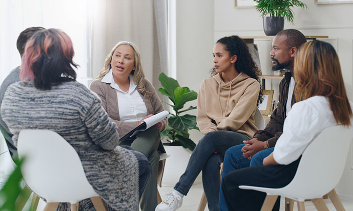 A group of six people depicted talking in a circle fashion