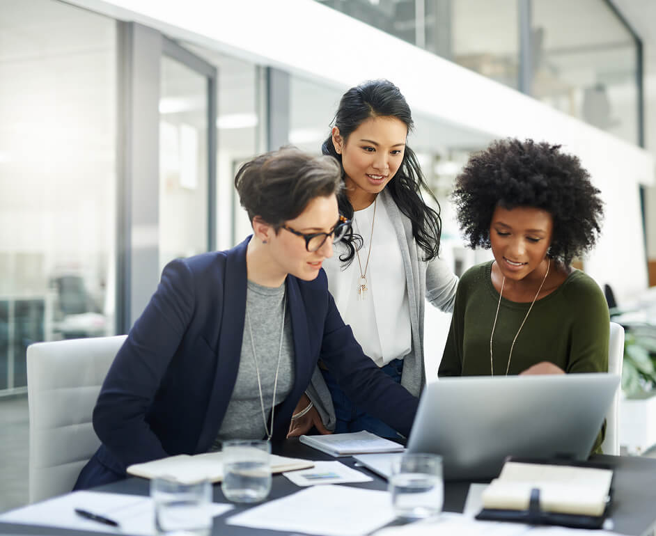 Three women review their talent pipeline on their laptop at a conference table.